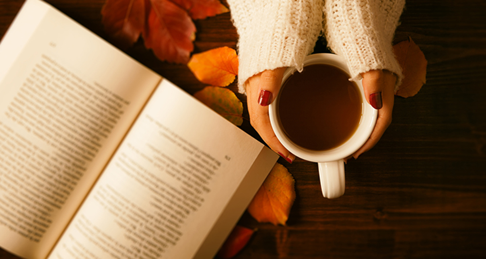 Woman hands holding teacup and opened book seen from above in vintage style