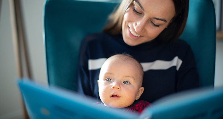 Baby Son Sitting On Mothers Lap Reading Story Book Together